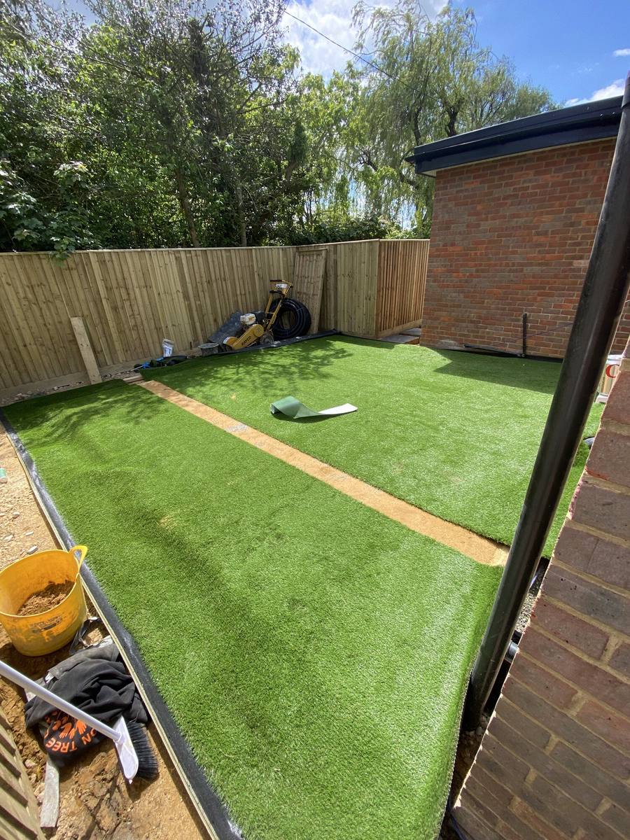 Artificial lawn with a putting green cut into it, edged against a fence