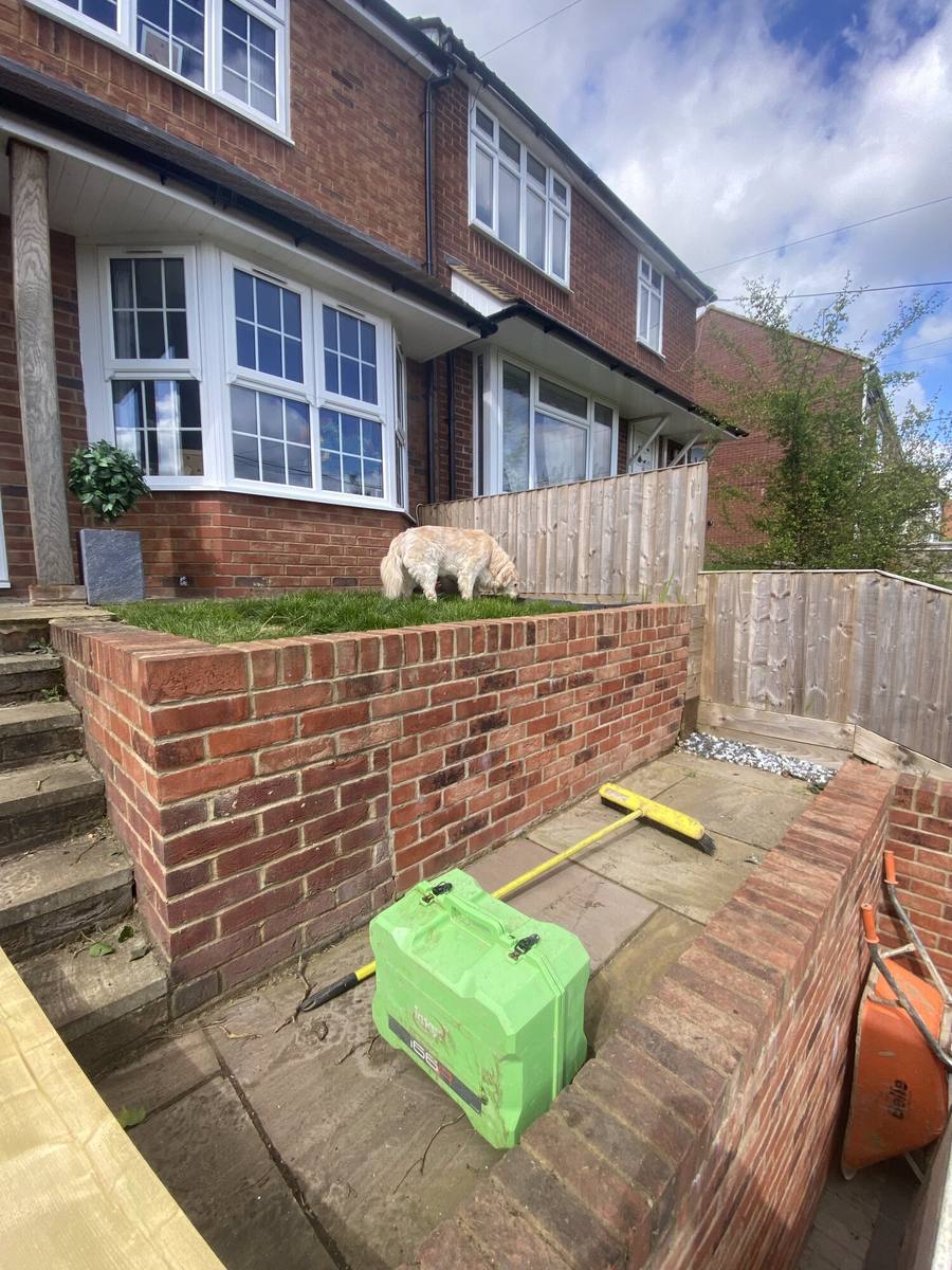 New brick retaining wall built against a house with a laser level set up