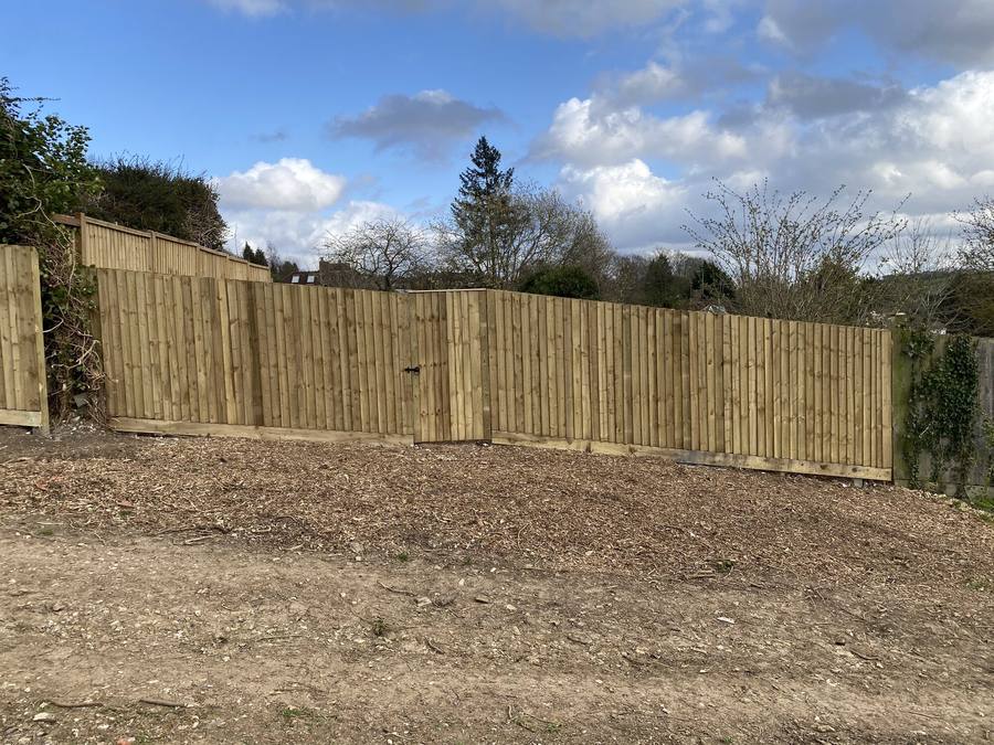 Long run of new close-boarded fencing across the back of a garden with a view beyond