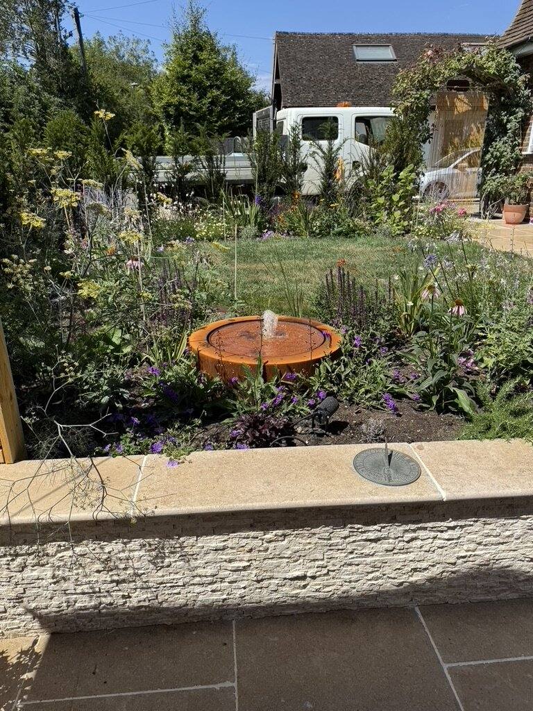 Corten steel water bowl set in a planted border above a stone-faced retaining wall
