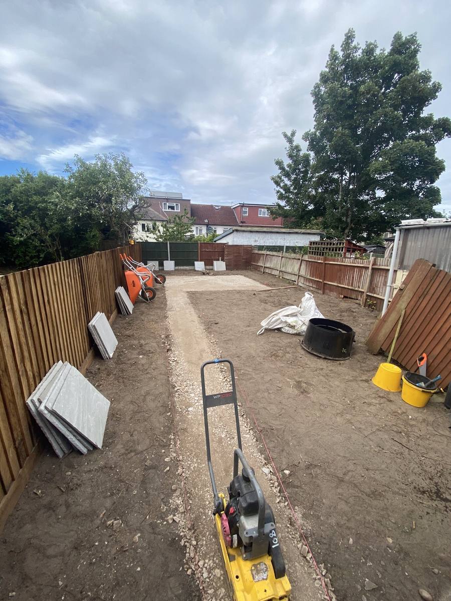 Cleared garden between fences with a wacker plate and materials on site