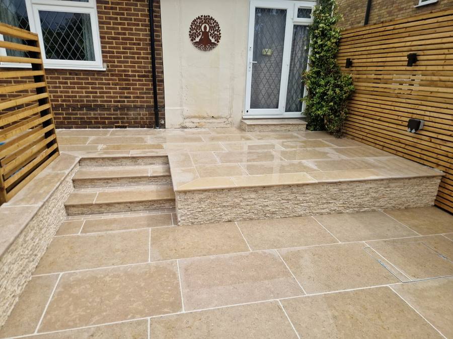 Beige limestone patio with two shallow steps up to a back door, a stone-faced riser and cedar slatted screens either side
