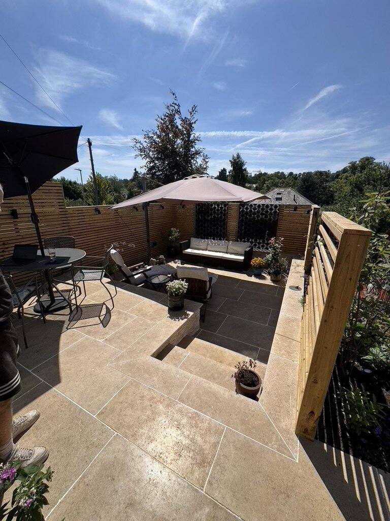 Limestone terrace with an outdoor sofa, parasol and dining set, enclosed by timber slatted screens