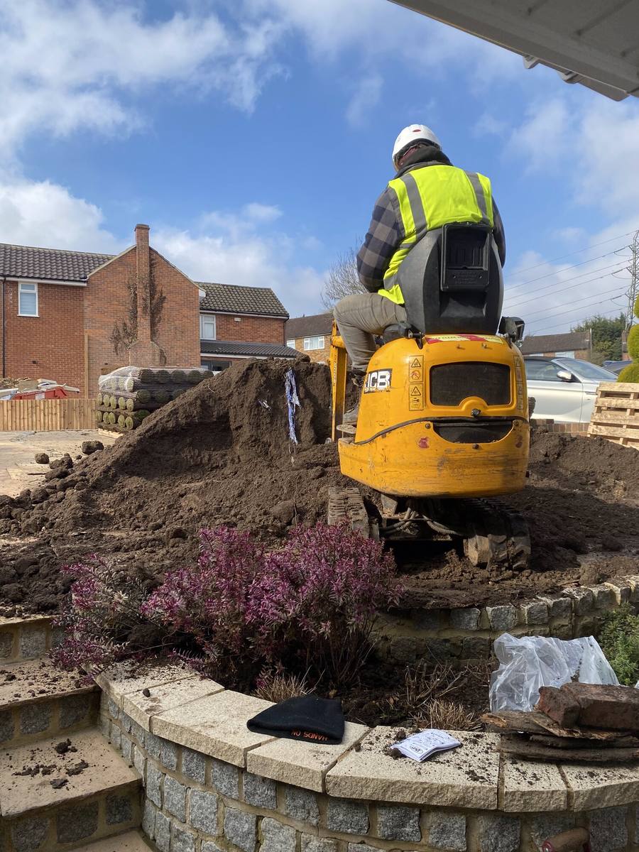 Operative in a hi-vis vest working a mini excavator over a raised border