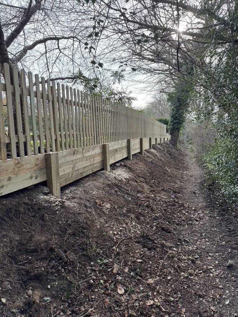 Picket fencing following the line of a steep bank beside woodland