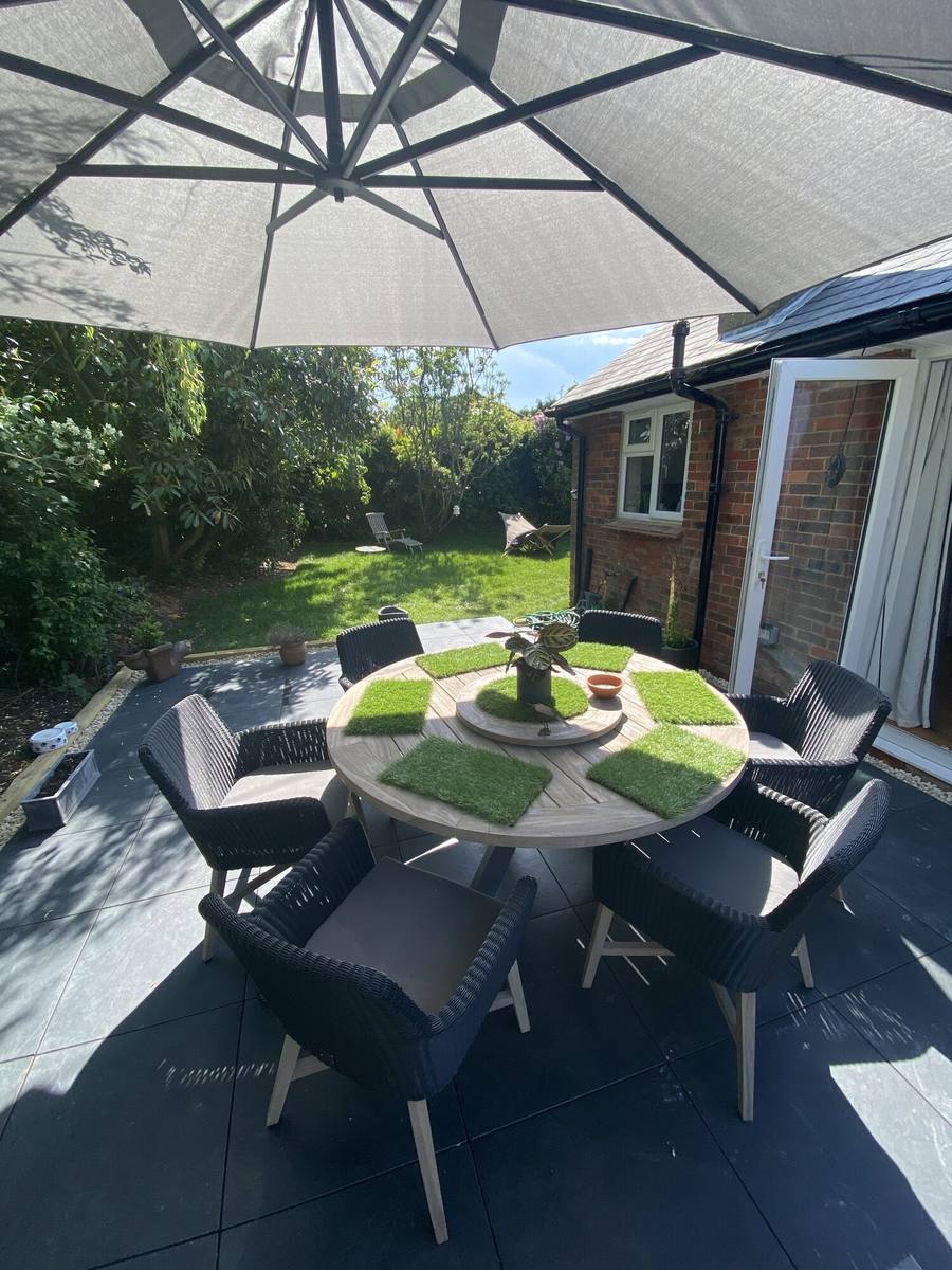 Round dining table and chairs under a large parasol on a dark porcelain terrace