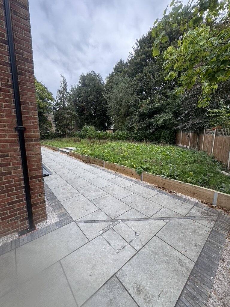 Grey porcelain path beside a brick wall with a newly planted border