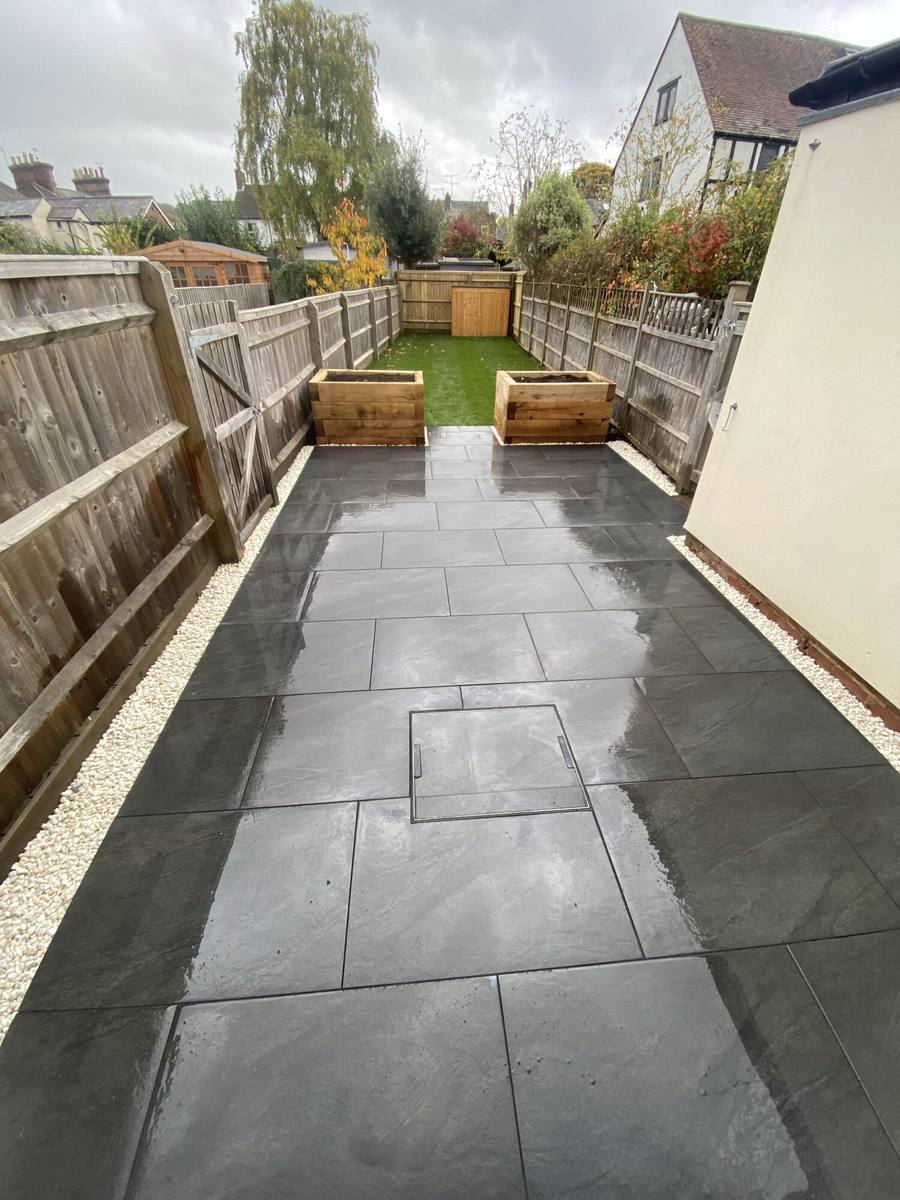 Long grey porcelain patio running the length of a fenced garden