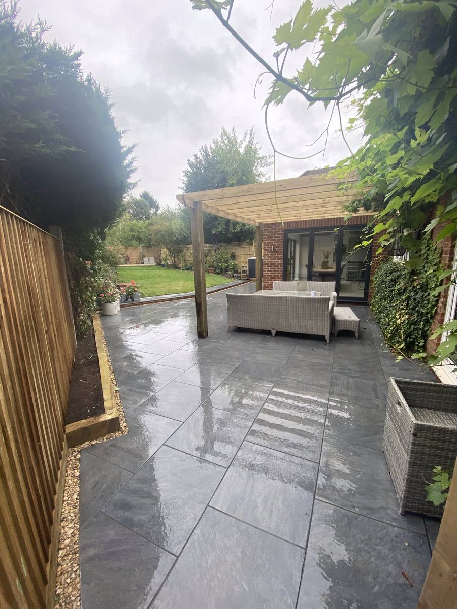 Grey porcelain patio with pergola, looking down the garden towards a lawn