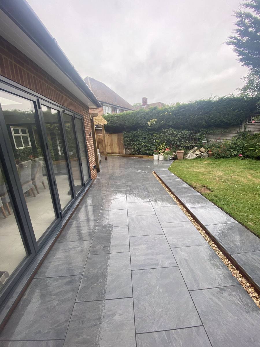 Grey porcelain paving running past bifold doors with a lawn alongside