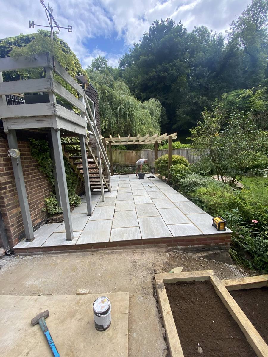 Porcelain paving being laid below a raised timber deck and pergola