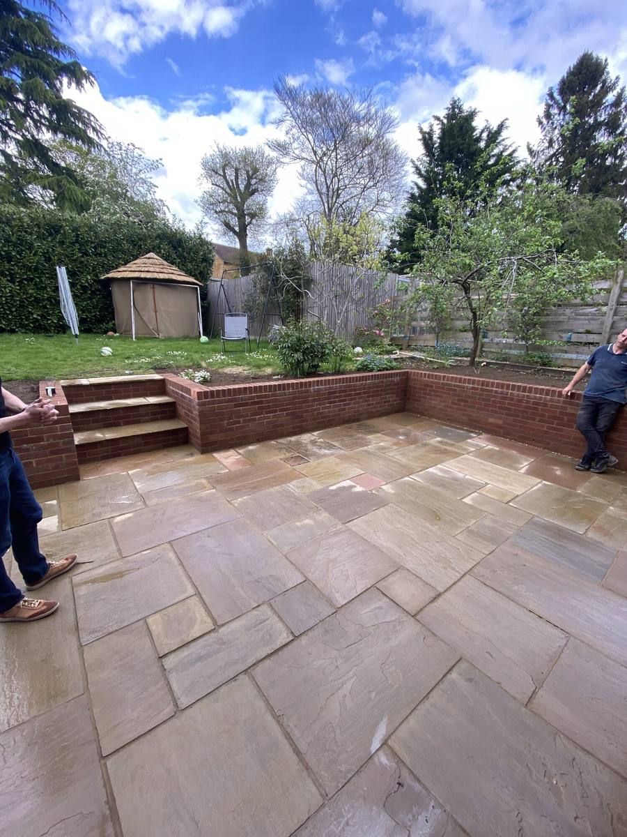 Riven sandstone patio enclosed by a low brick retaining wall with steps to a lawn