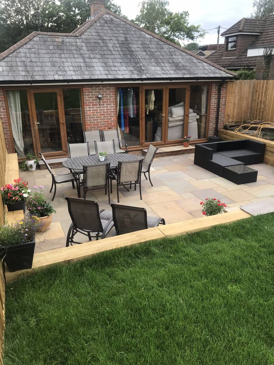 Sandstone patio and lawn in front of a garden room with bifold doors