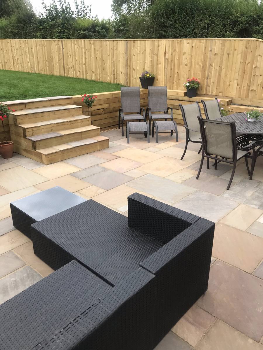 Sandstone patio with steps up to a raised lawn, outdoor furniture in the foreground