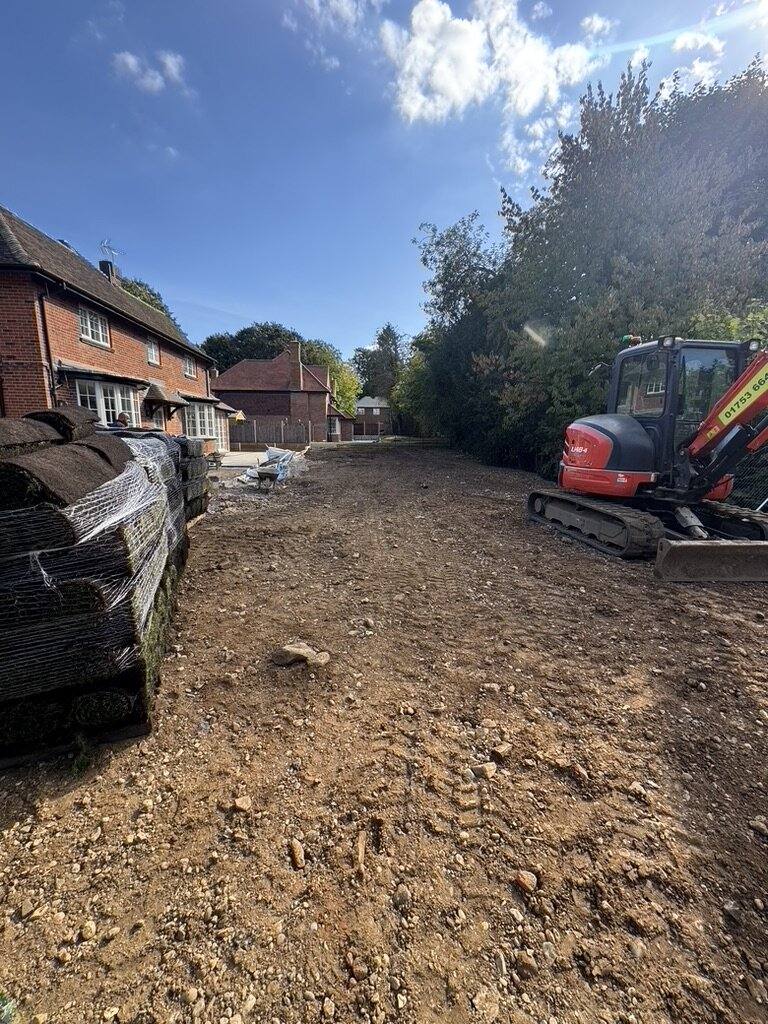 Large garden stripped back to soil with an excavator and stacked materials