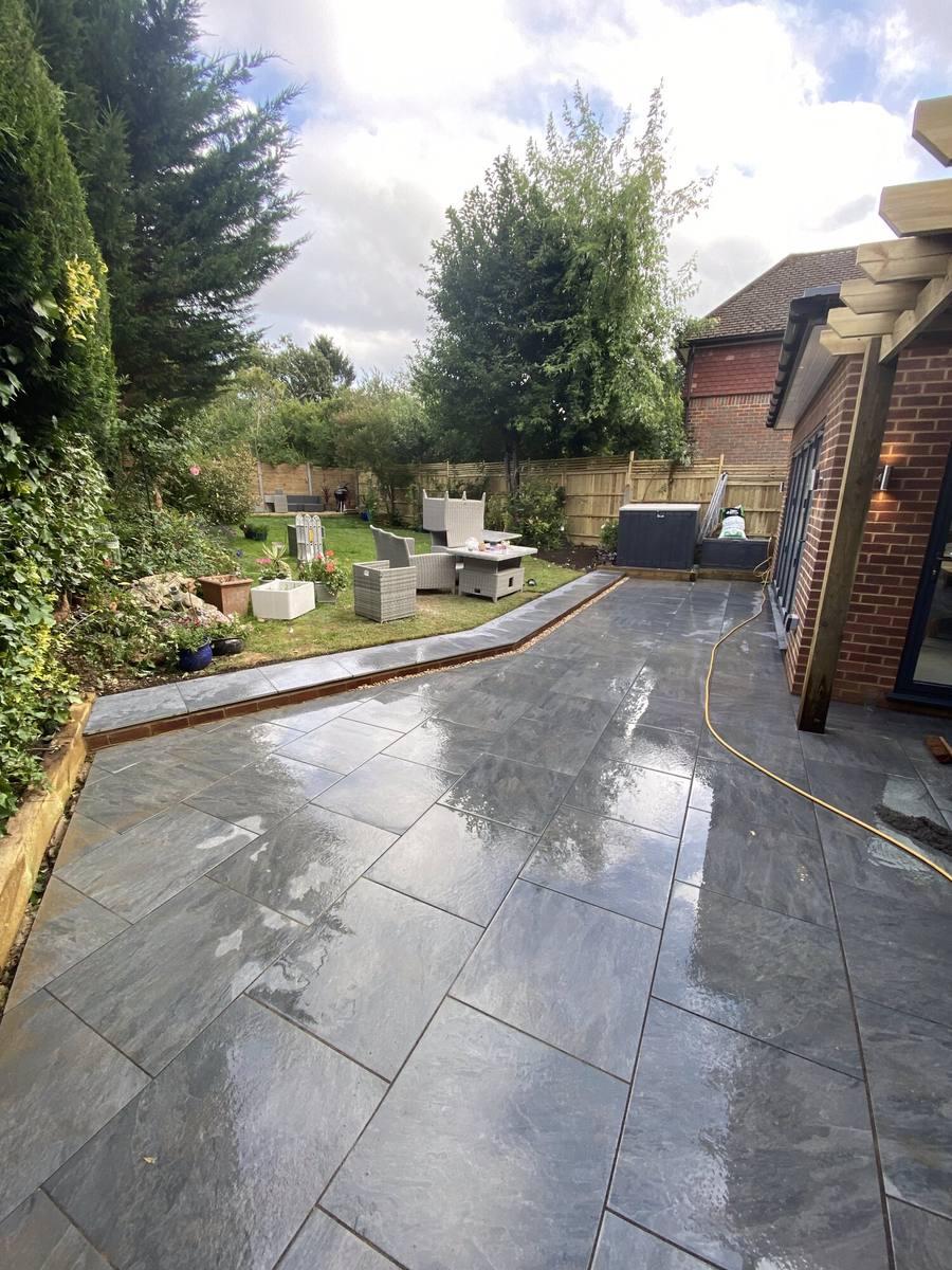 Dark slate-grey patio in a sloping garden with a raised bed and steps