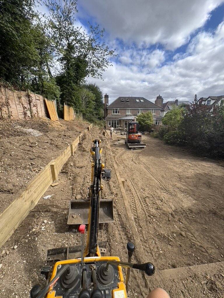 Excavator working along a trench with timber sleeper retaining going in behind it