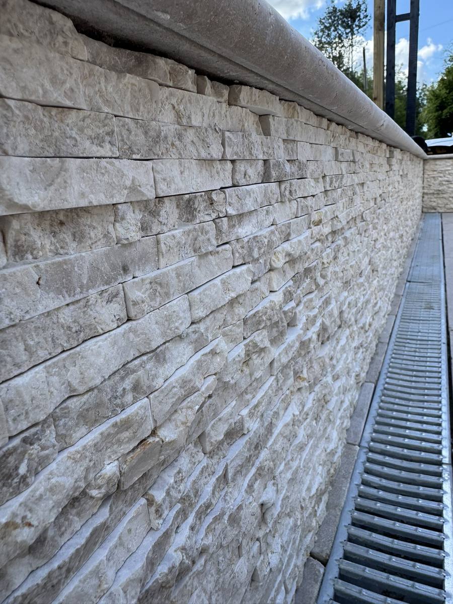 Stone-clad retaining wall with a channel drain running along its base