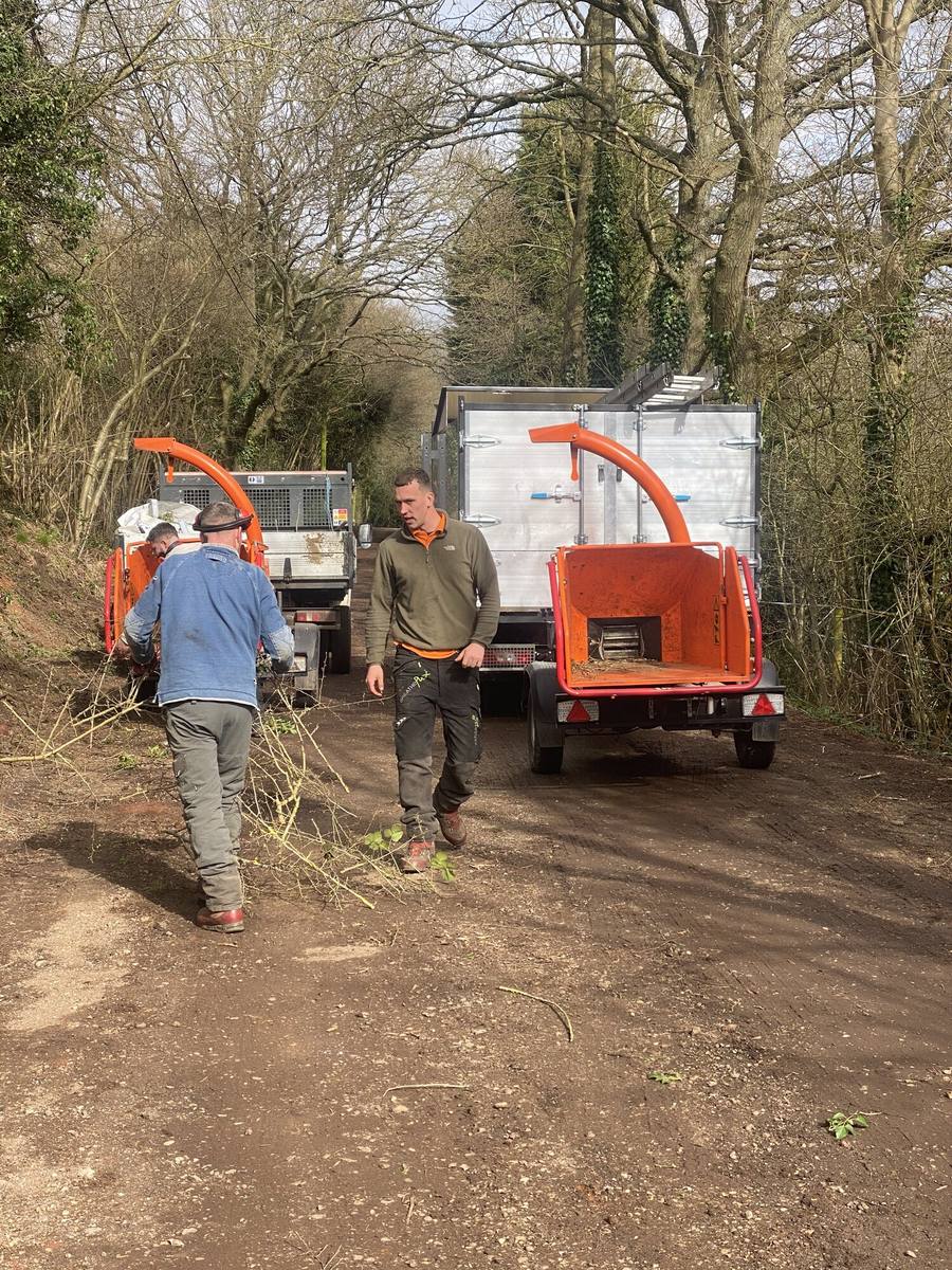 Two of the team working at a chipper behind a tipper truck on a track