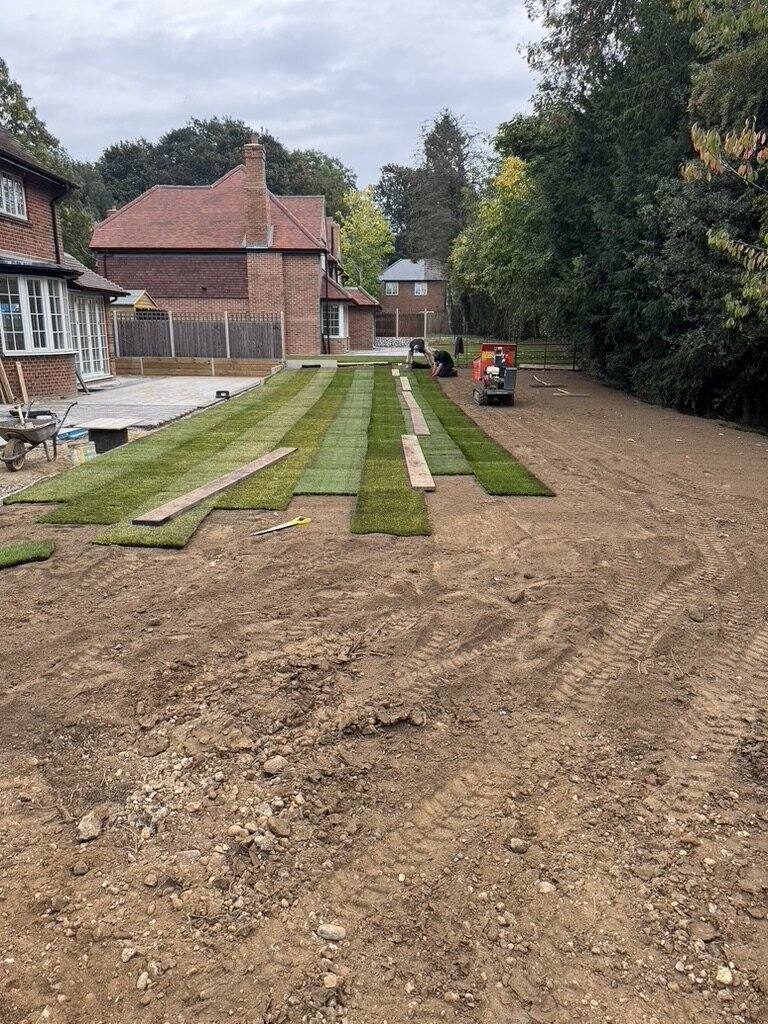 Rolls of new turf part-laid across a prepared and levelled garden